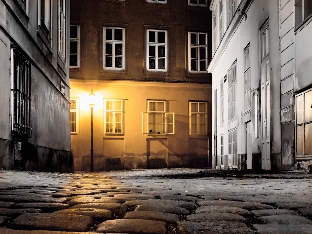 Foggy old European cobblestone street at night with a glowing vintage street lamp